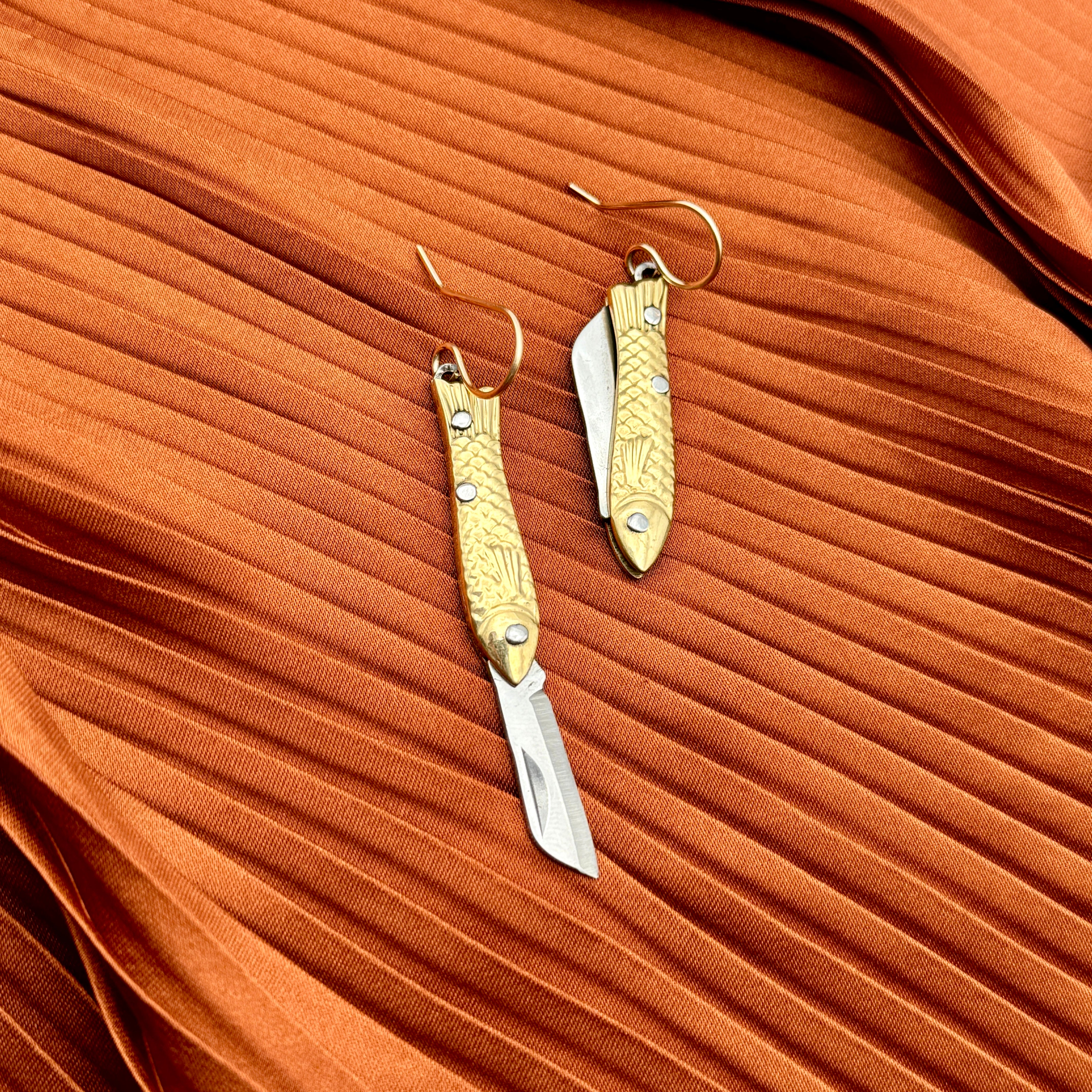 A pair of earrings featuring gold-colored miniature fish shaped utility working pocket knife on a 14 karat gold fill ear wire
