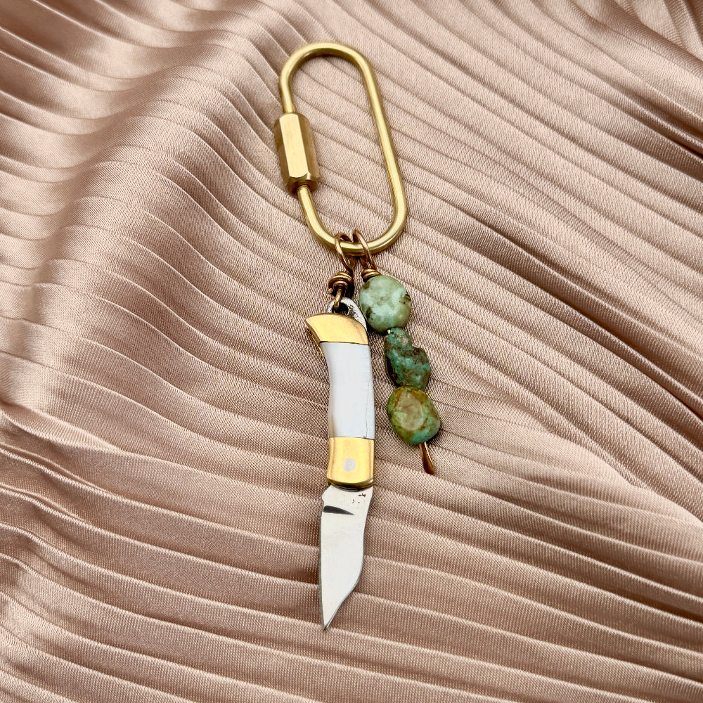 Gold keychain purse charms with mini knives and turquoise beads on a beige background