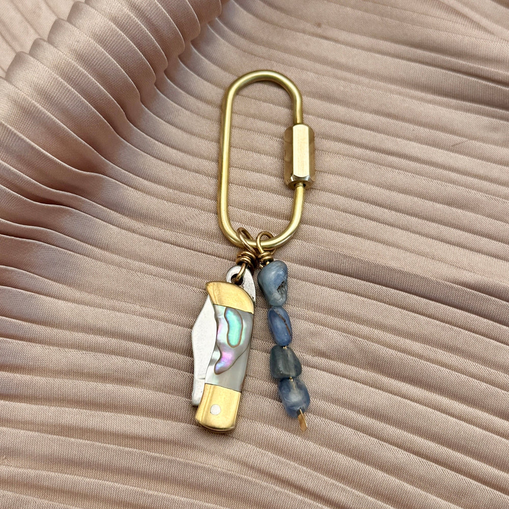 Gold keychain purse charm with decorative elements on a beige fabric background