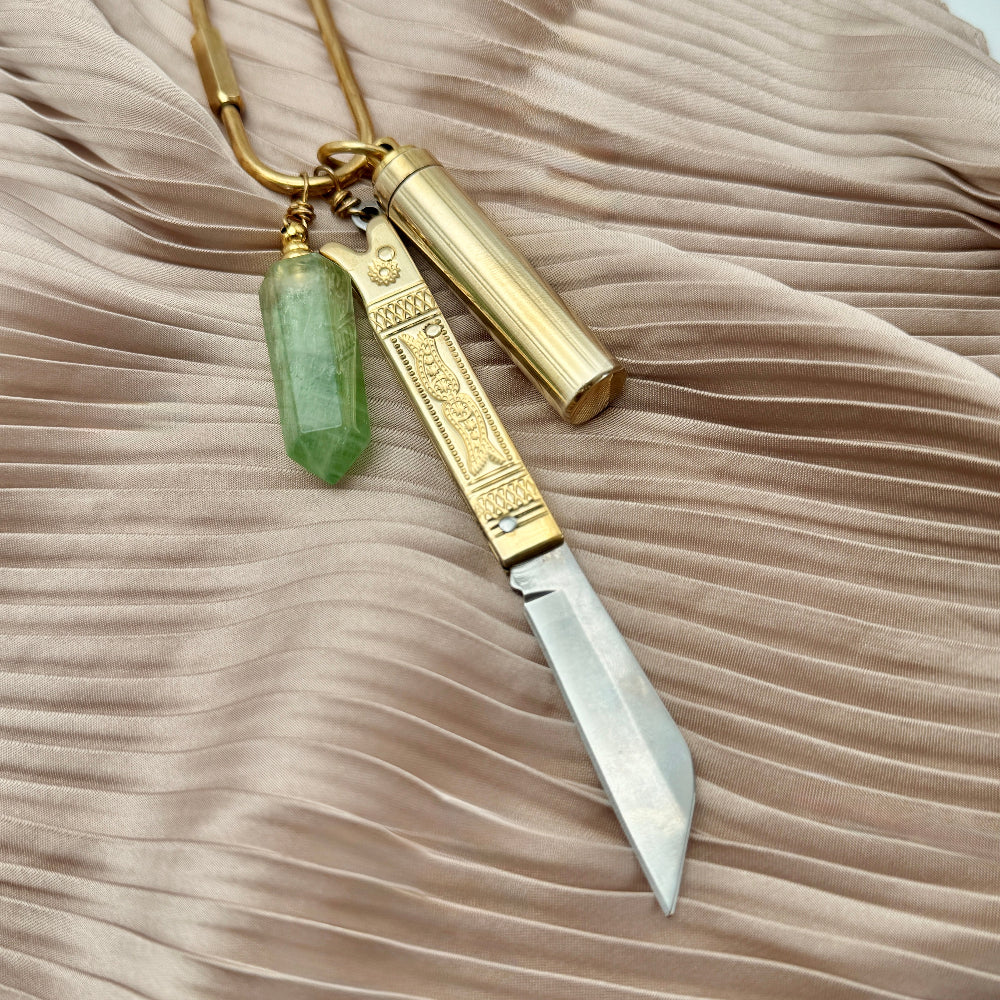 Small tool with gold handle and green stone on a beige fabric background