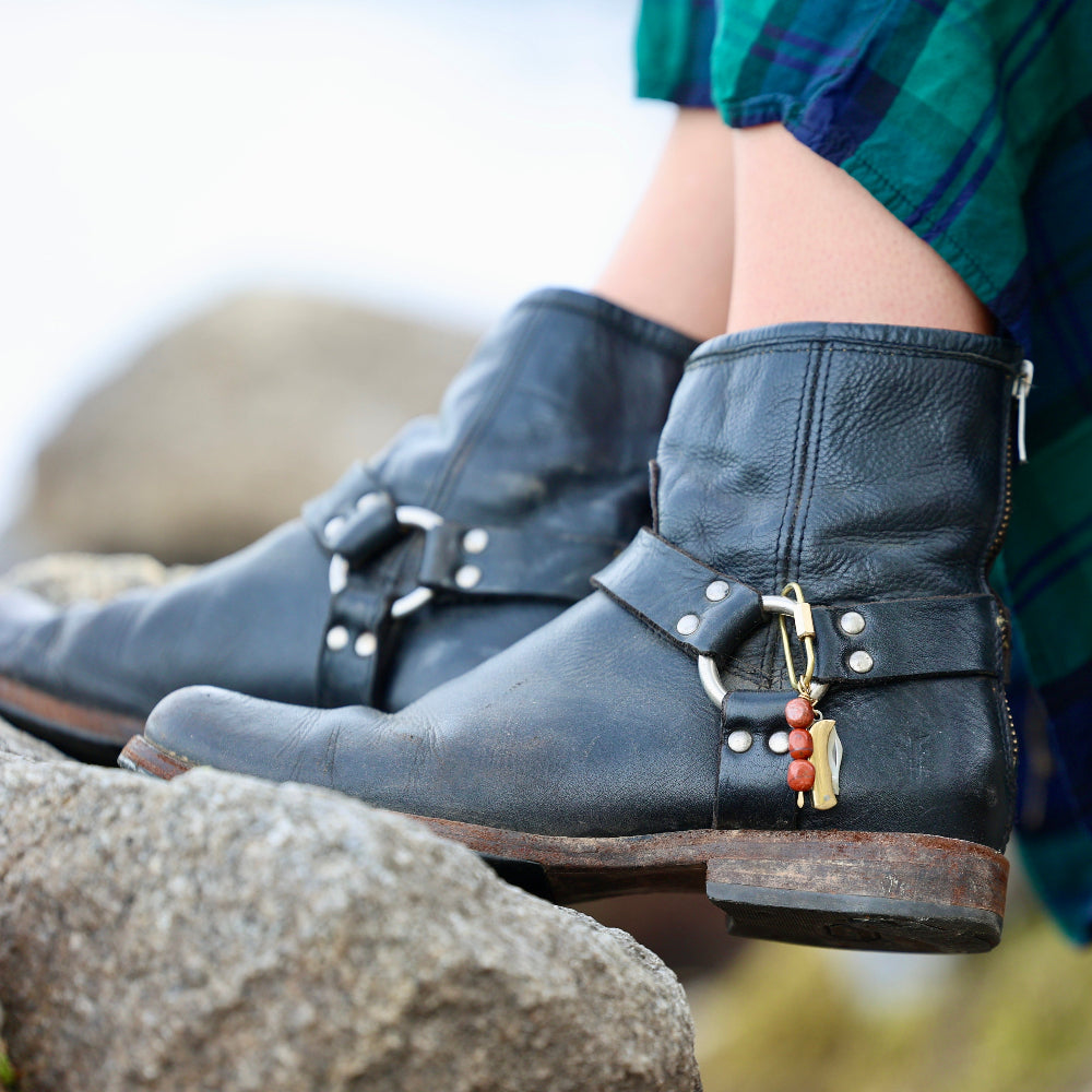 Person wearing black leather boots with a charm clipped onto the boot buckle.