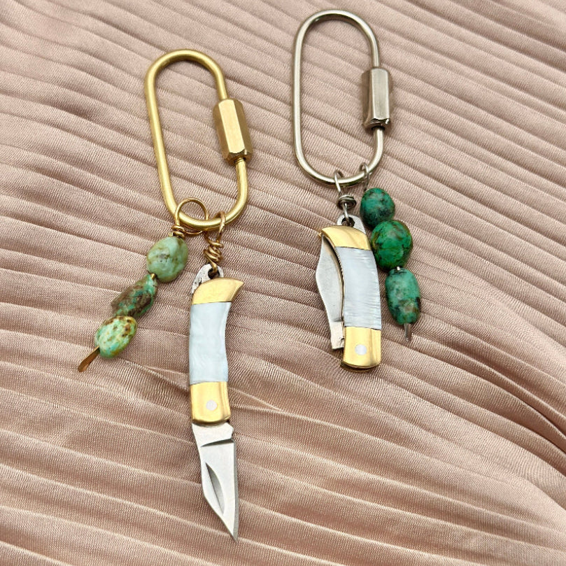 gold and silver keychain purse charms with mini knives and turquoise beads on a beige background