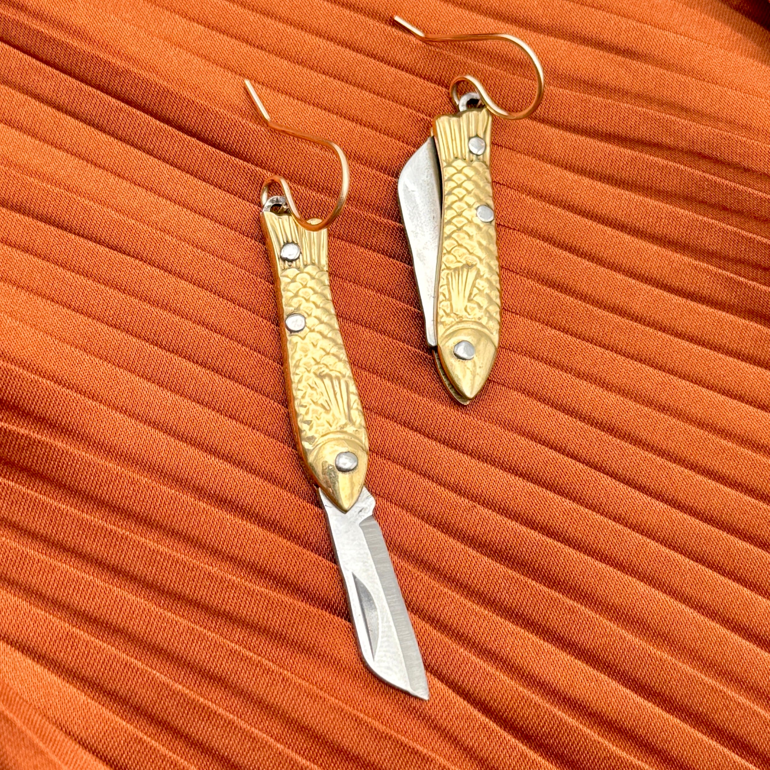 A pair of earrings featuring gold-colored miniature fish shaped utility working pocket knife