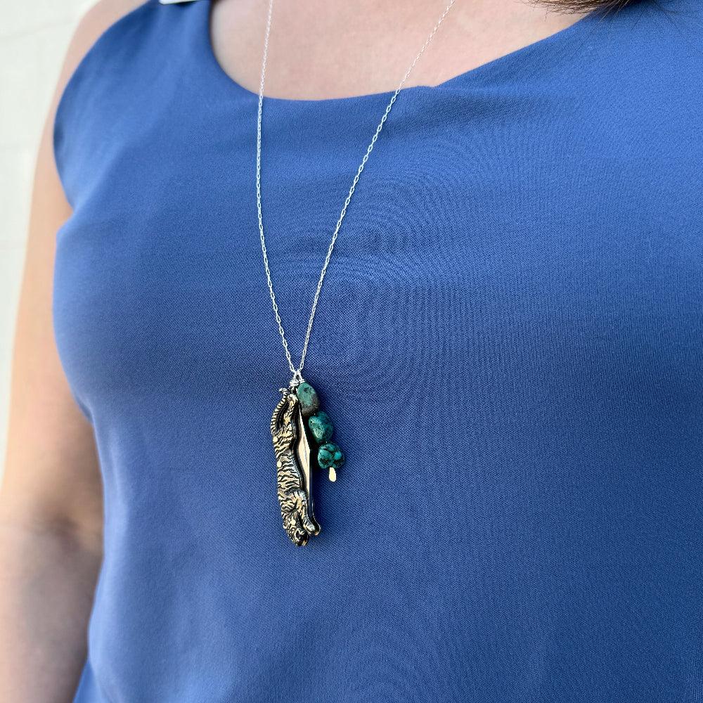 Person wearing a blue top with a necklace featuring a tiger shaped pocketknife on a silver chain