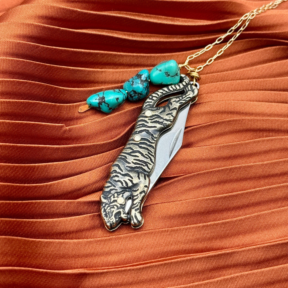 Necklace with tiger-shaped pocketknife pendant and turquoise beads on orange fabric background