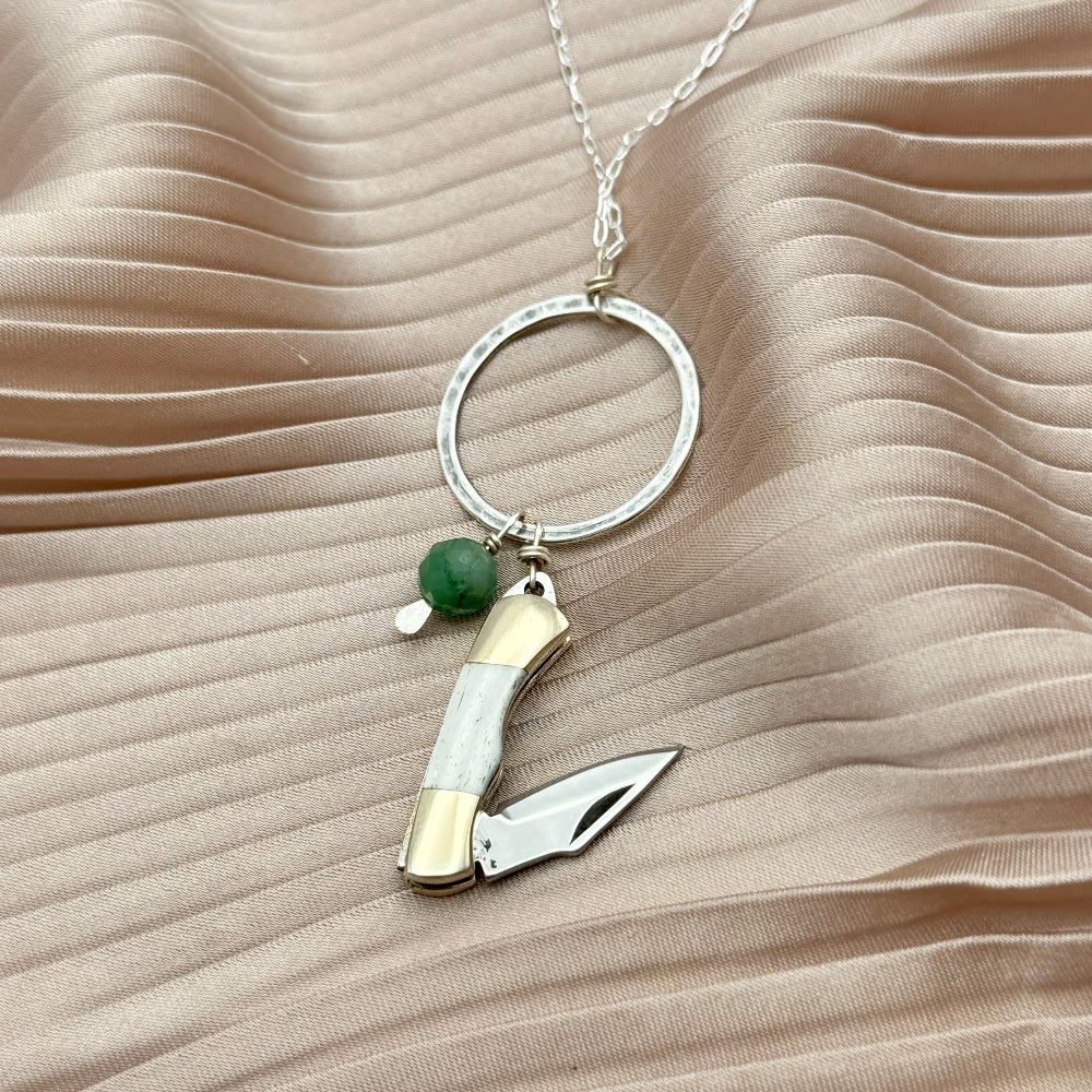 Necklace with miniature bone pocketknife and emerald bead hanging from round pendant
