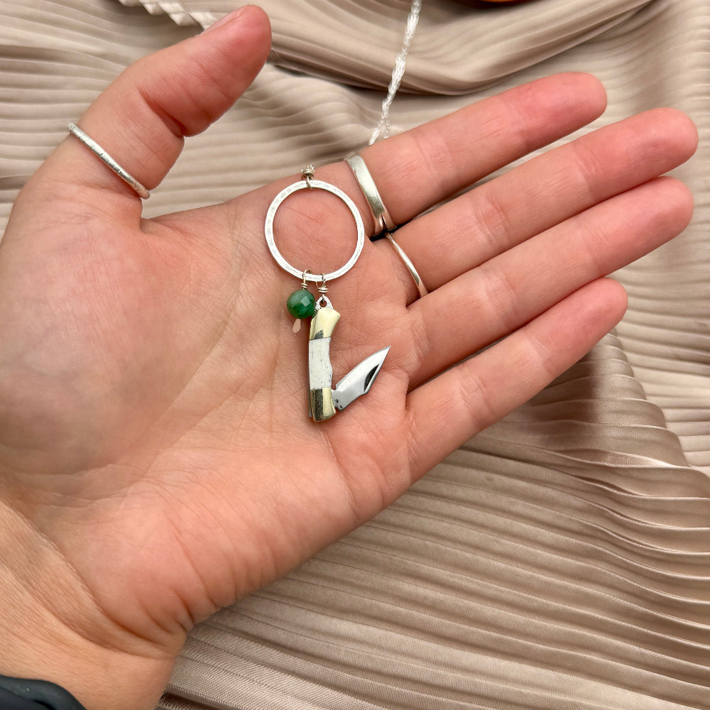 Necklace with miniature bone pocketknife and emerald bead hanging from round pendant