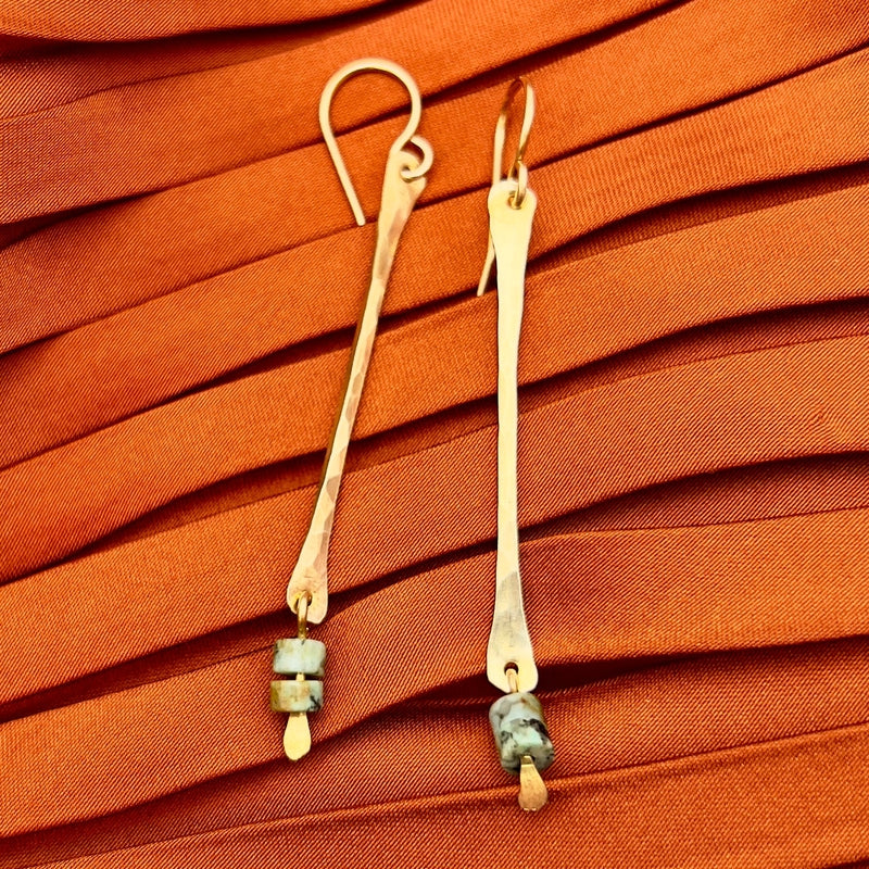 The Spark Earrings by Fluff Hardware are long, slender hammered sterling silver earrings with small stone beads on the ends, shown on textured orange fabric. Hypoallergenic and ideal for sensitive ears.