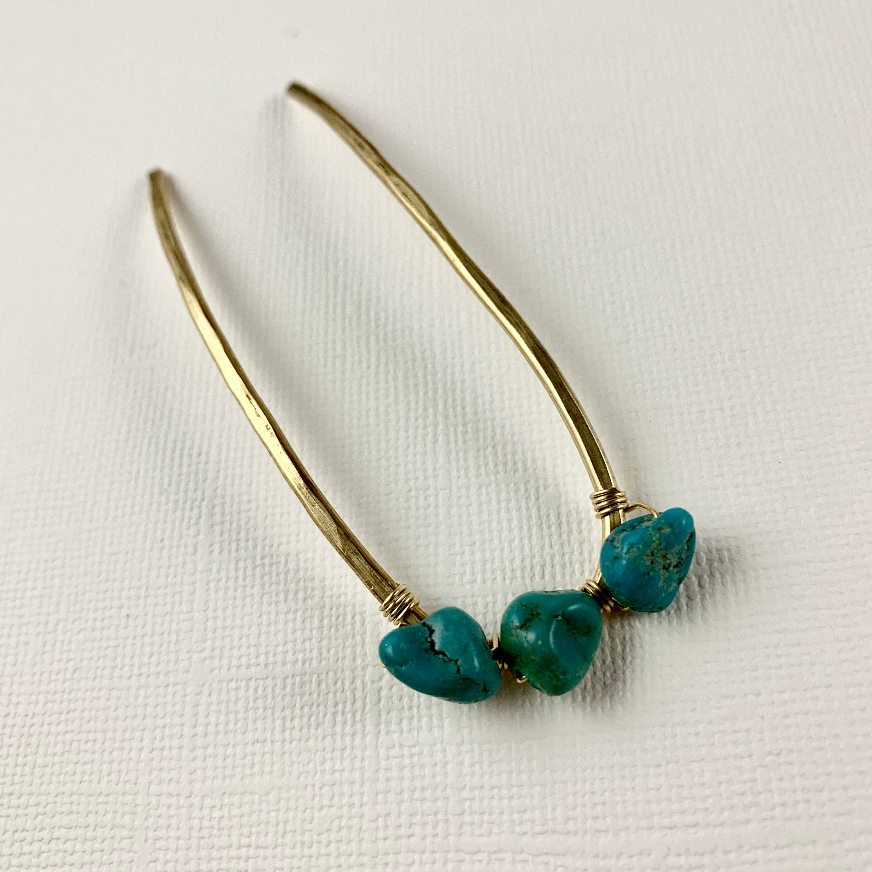 The Fluff Hardware Turquoise Hair Fork features gold-tone curved metal accented with three irregularly shaped turquoise beads, shown against a textured white background.