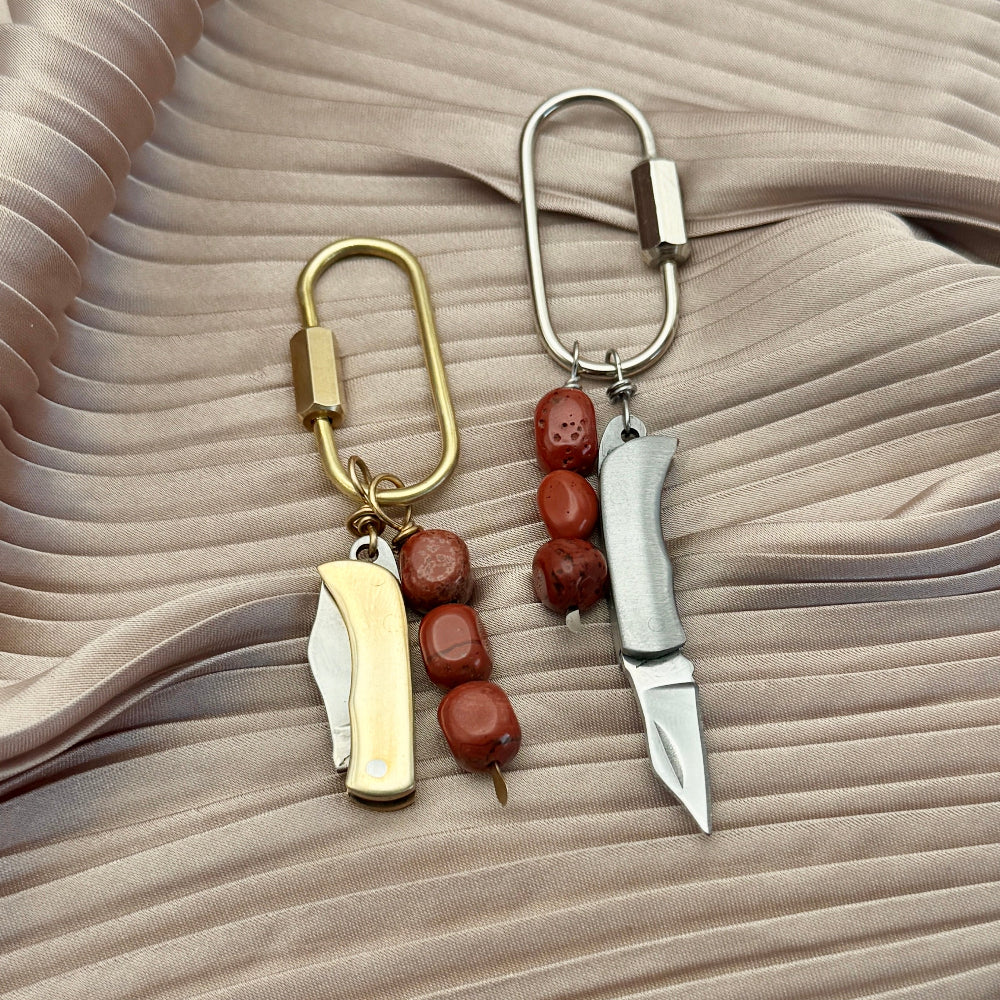 Two keychain purse charms with gold and silver blades on a beige fabric background