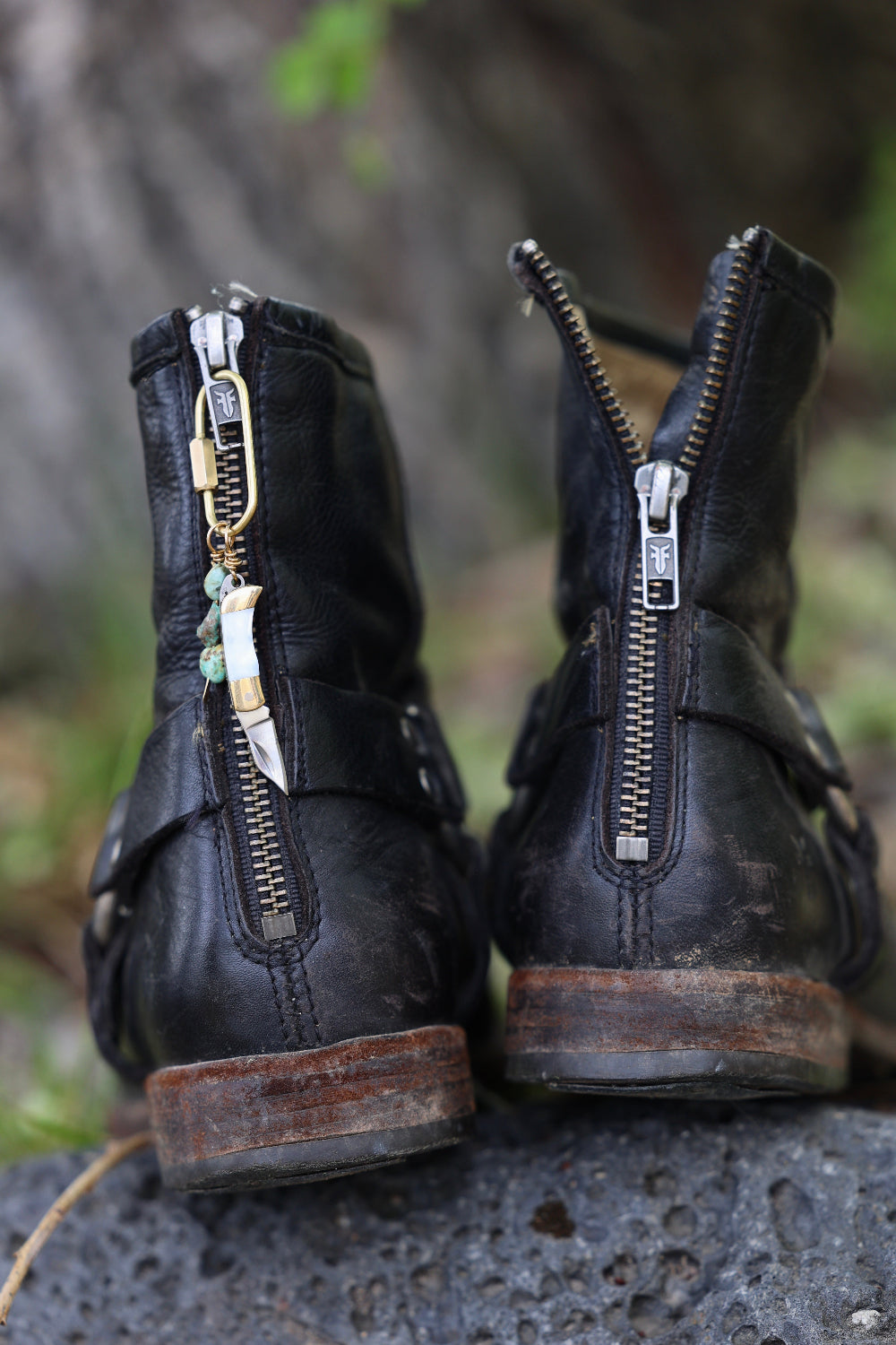Pair of black leather boots with a mini charm on the zipper.