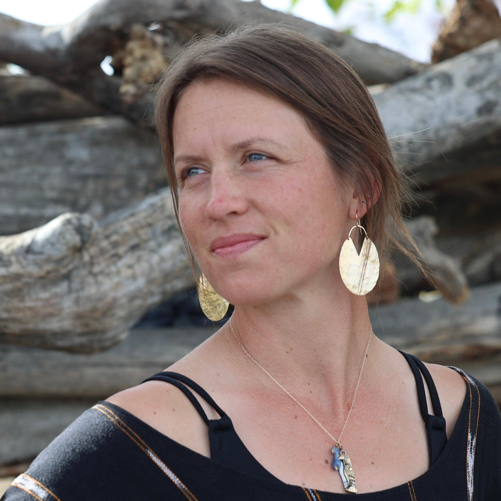 Woman wearing gold earrings and a necklace with a black top against a natural background