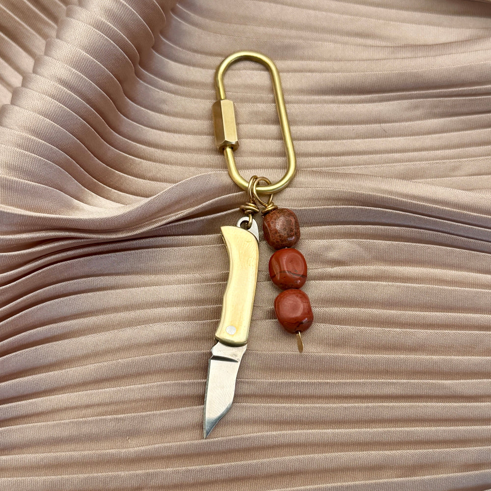 Keychain purse charm with knife and beads on a pleated fabric background