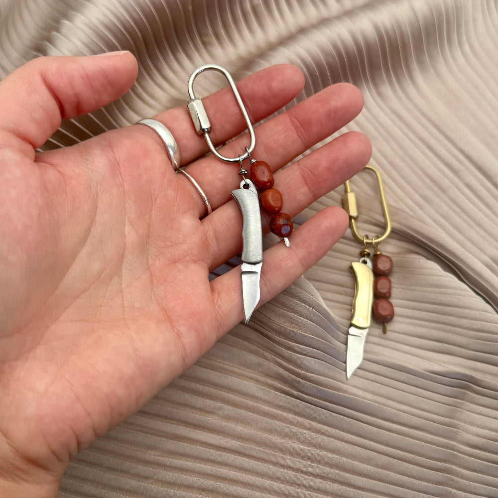 Hand holding two blade-shaped keychains with beads on a textured surface