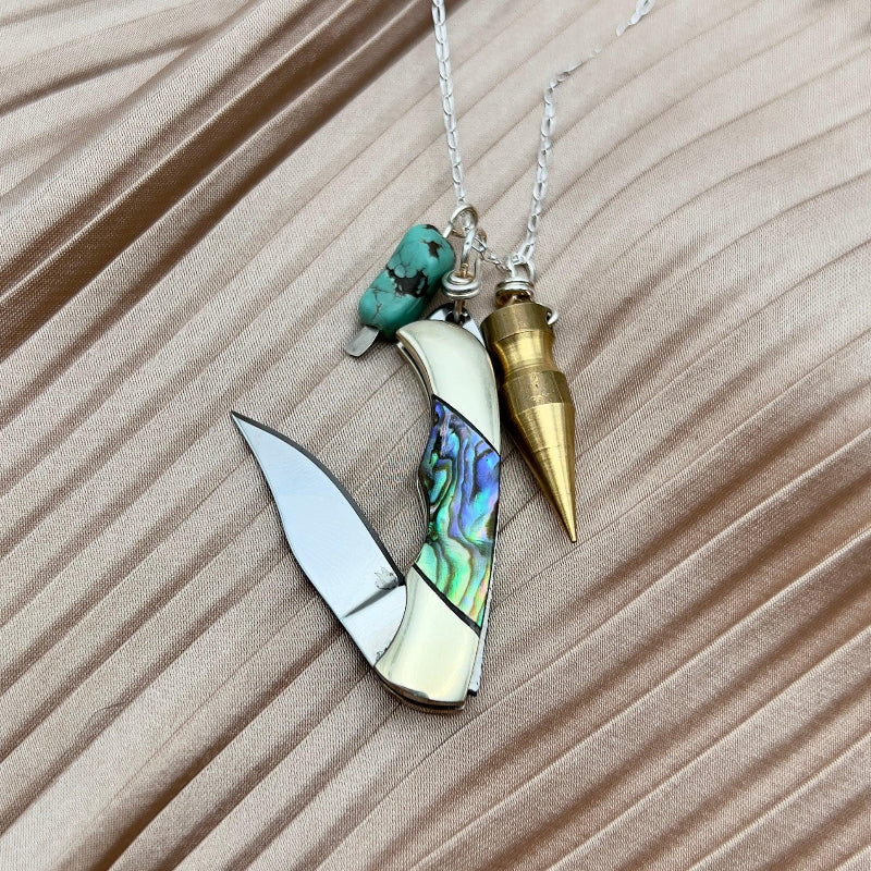 A multi-functional pendant necklace with a silver chain, featuring a pocket knife design with an abalone shell inlay and a genuine turquoise stone, accompanied by a brass bullet