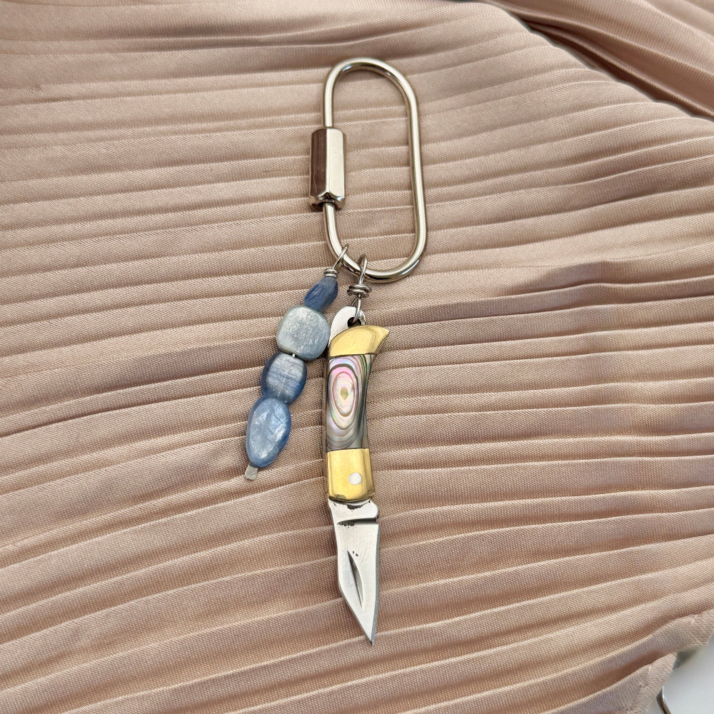 Keychain purse charm with knife and beads on a beige fabric background