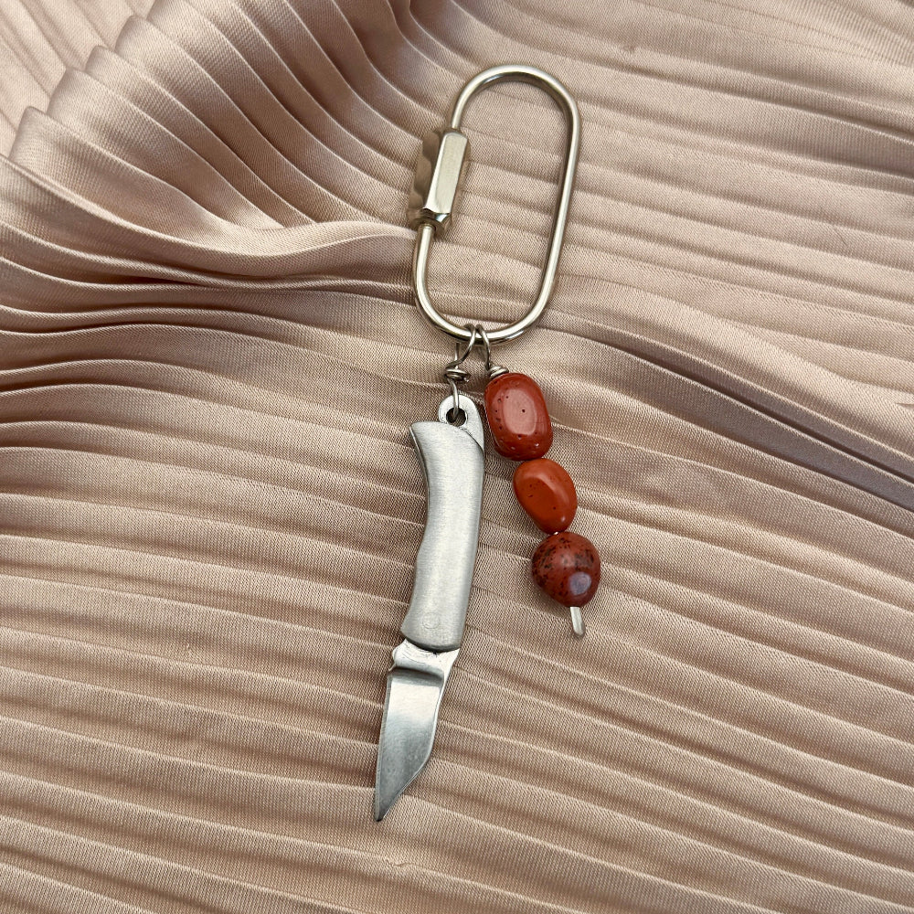 Keychain purse charm with blade and beads on a beige fabric background