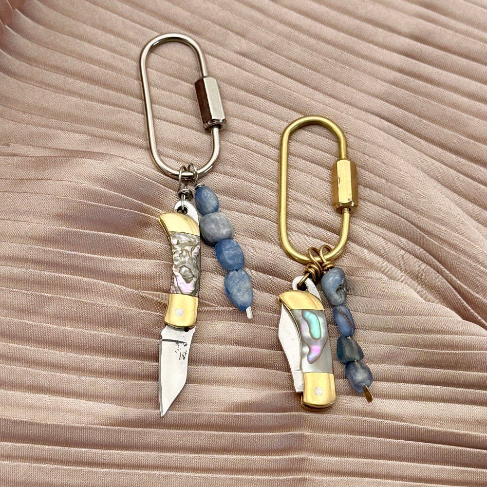 Two keychain purse charms with knife designs on a textured beige surface