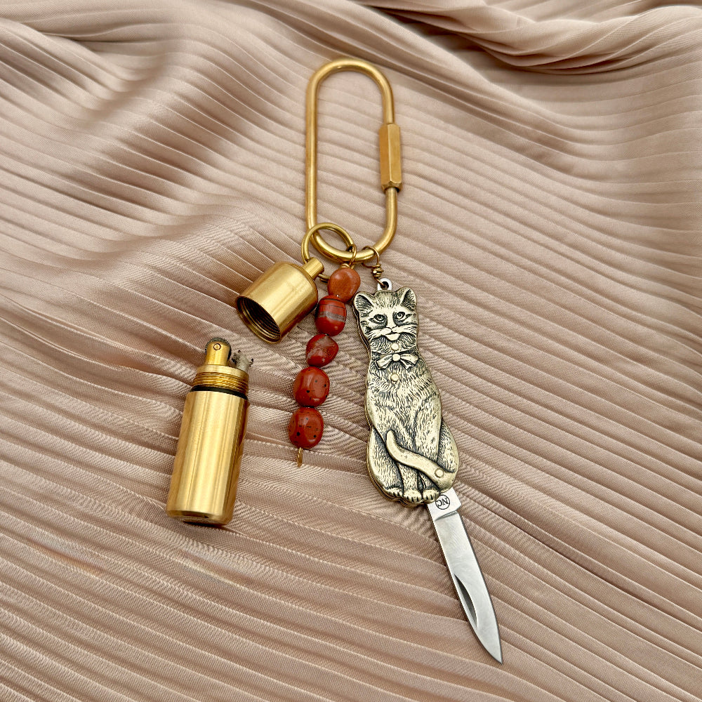 purse charm with cat design, lighter, and and small jasper beads on a fabric background