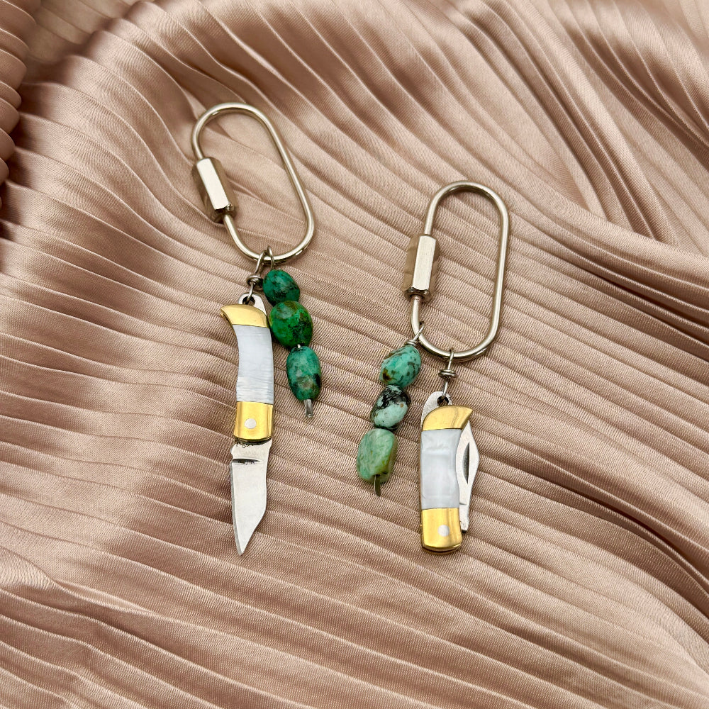 gold and silver keychain purse charms with mini knives and turquoise beads on a beige background