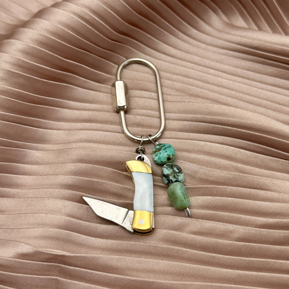 mini purse charm with tool and turquoise stones on a beige fabric background