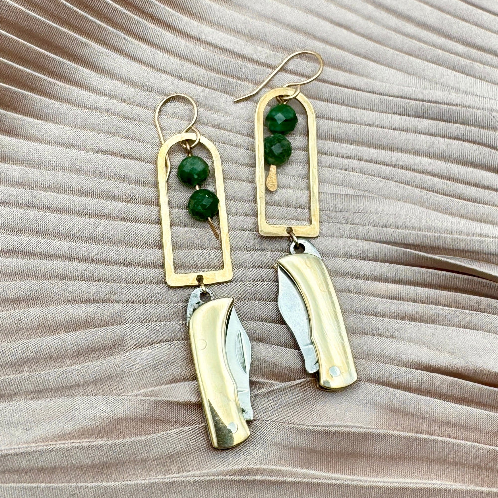 Gold Metal Billie Mini Pocket Knife dangling from rounded top frame with two faceted emerald beads hanging from ear wire