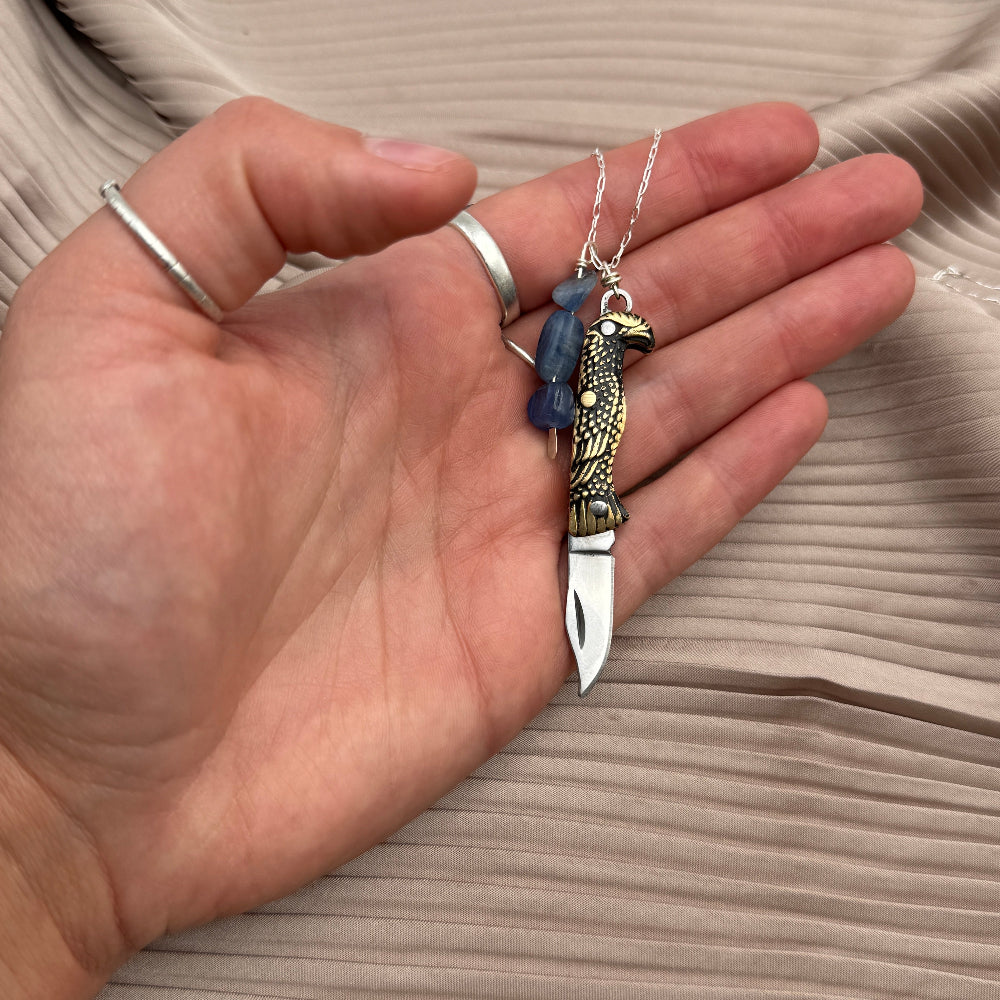 Hand holding a  bird shaped pocketknife-shaped pendant with blade open on a beige fabric background