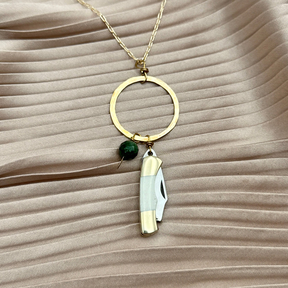 Necklace with miniature bone pocketknife and emerald bead hanging from round pendant